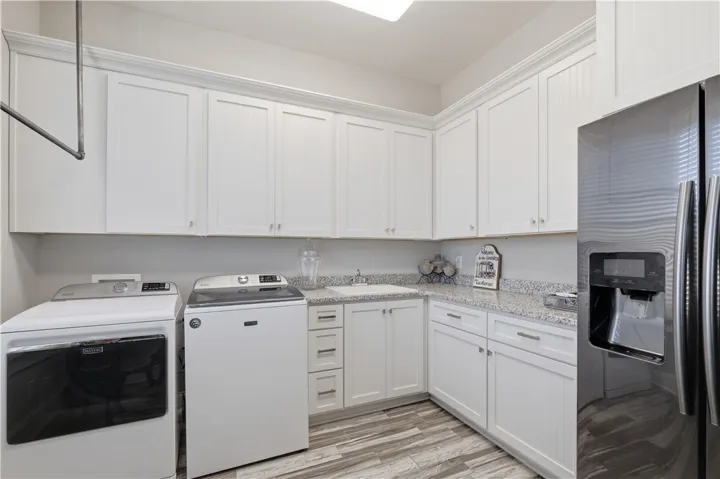 The laundry room is exceptionally well appointed. Extensive cabinetry, a second refrigerator, a utility sink, hanging bar, and abundant counter space make it feel more like a secondary kitchen than a utilitarian space.