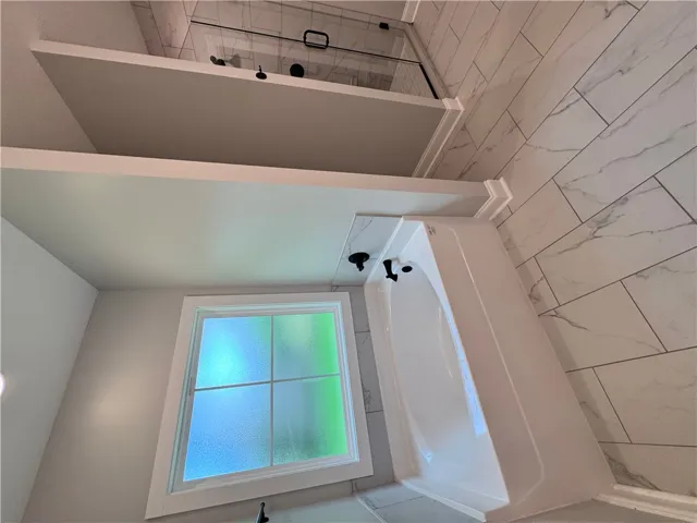 This bright bathroom features a clean tub, a window for natural light, and tiled walls for a refreshing feel.