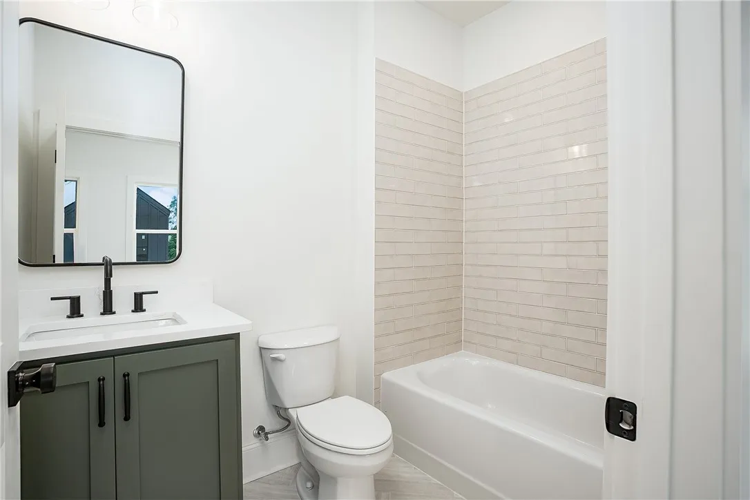 A sleek vanity with a dark green cabinet and modern fixtures complements the tiled shower and bath.