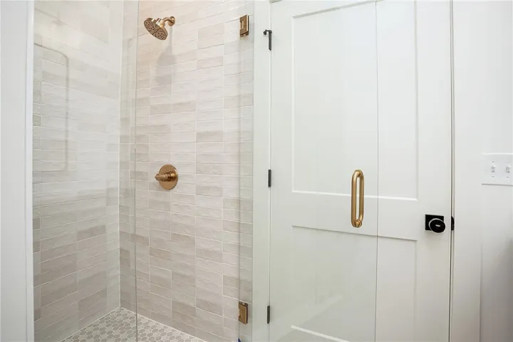 Elegant shower featuring brass fixtures and a textured tiled wall and floor.