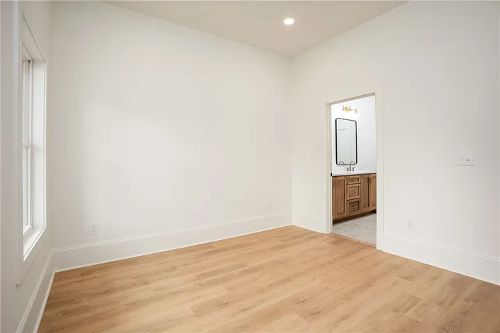 A well-lit bedroom features durable hardwood flooring, leading into a private en suite bathroom.