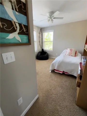 A well-lit room offers cozy comfort with soft carpeting and natural light from ample windows.