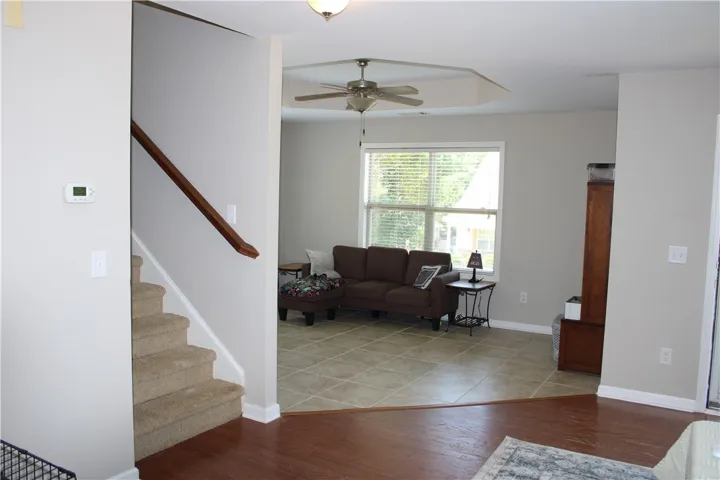Natural light filters into this inviting living area featuring a ceiling fan and a staircase with plush carpeting.
