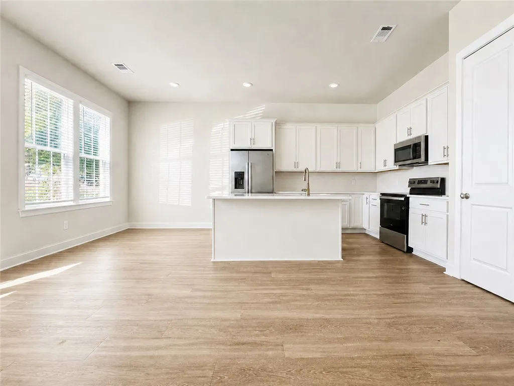 Generous windows illuminate an open kitchen featuring a central island and warm wood flooring.