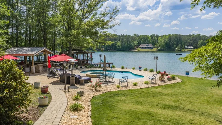 This tranquil lakeside retreat features a refreshing pool, spa, and a charming outdoor kitchen, all set against a beautiful natural backdrop.