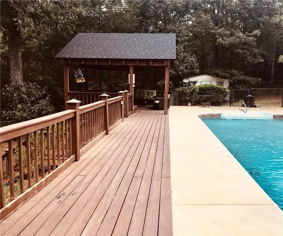 A spacious wooden deck with a covered sitting area with hot tub extends alongside a sparkling private swimming pool.