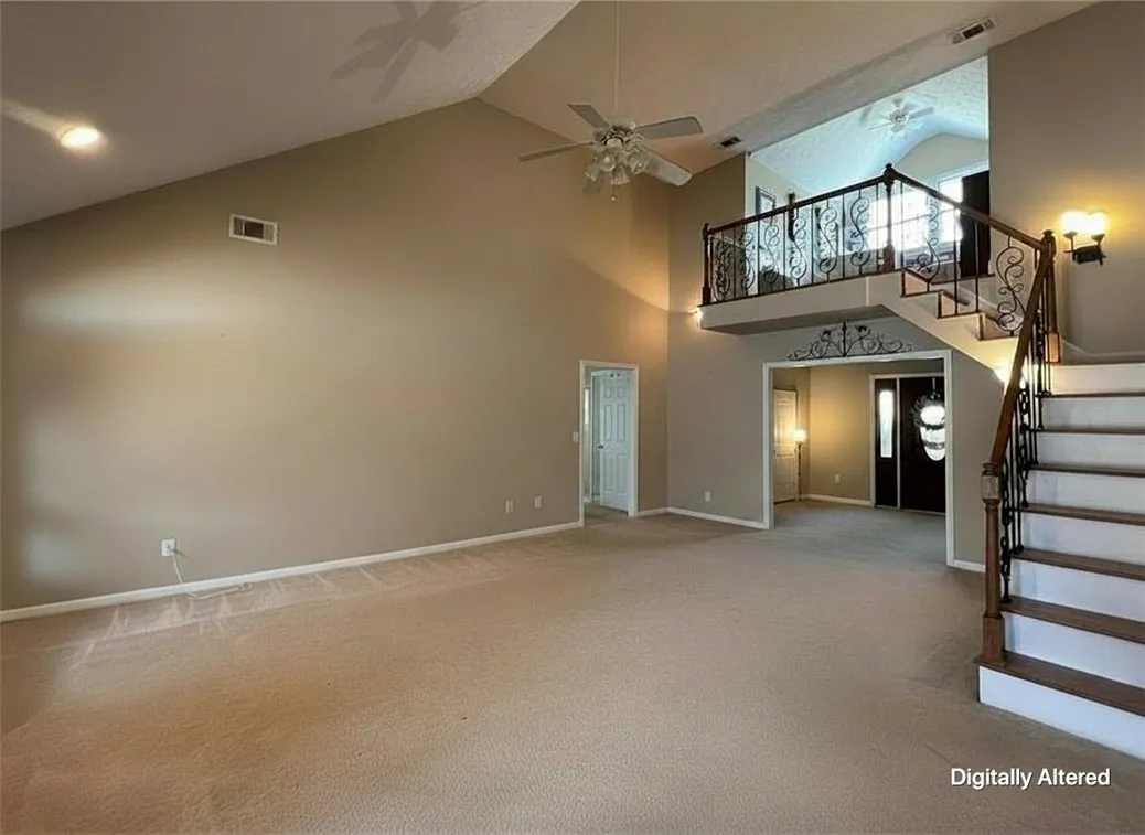 A spacious living area features soaring vaulted ceilings and an elegant wrought iron staircase leading to an upstairs balcony. 
Note: Photo has been digitally altered to showcase an empty space