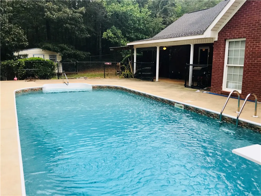 A sparkling pool invites relaxation, set against a backdrop of mature trees and a brick-accented dwelling.