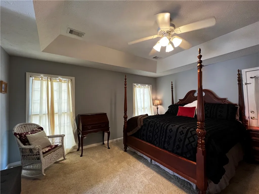 Relaxation awaits in this private primary bedroom featuring a tray ceiling and soft, neutral carpeting.