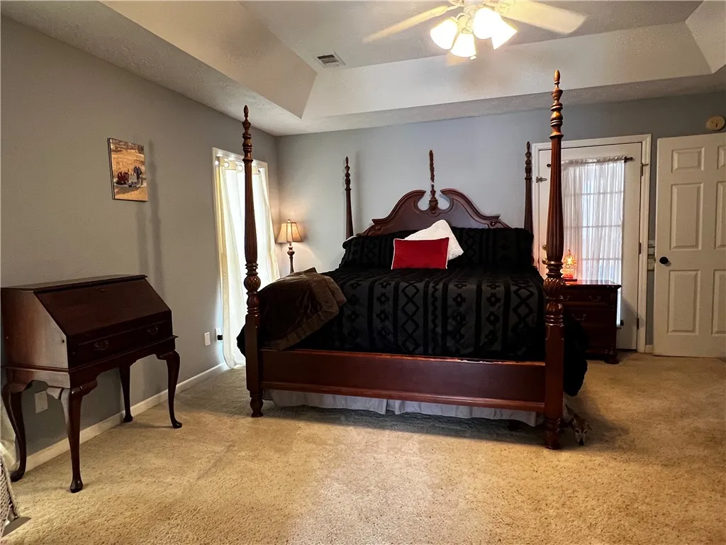A well-lit primary bedroom features a tray ceiling, ceiling fan, and ample space.