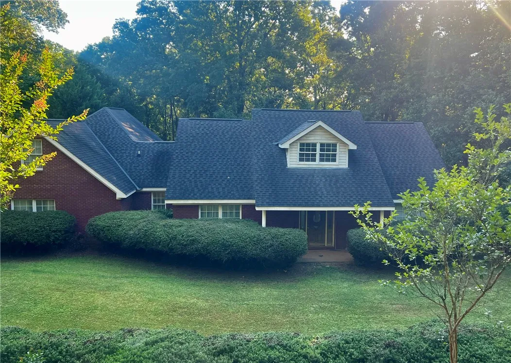 Mature trees and lush shrubbery enhance this appealing red brick residence, showcasing a well-maintained lawn.
