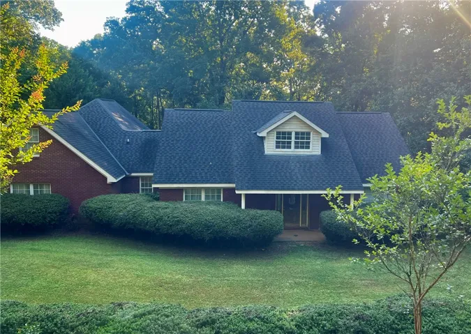 Mature trees and lush shrubbery enhance this appealing red brick residence, showcasing a well-maintained lawn.