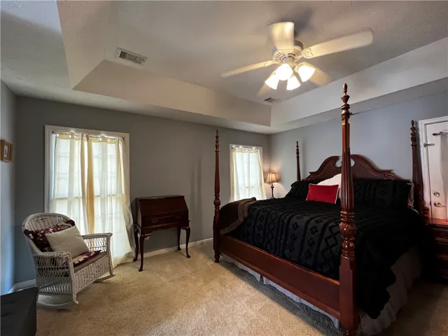 Relaxation awaits in this private primary bedroom featuring a tray ceiling and soft, neutral carpeting.