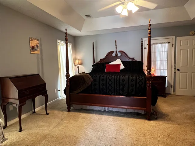 A well-lit primary bedroom features a tray ceiling, ceiling fan, and ample space.