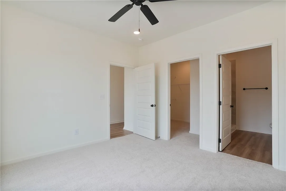 A spacious, newly finished room boasts clean carpeted flooring and a modern ceiling fan.