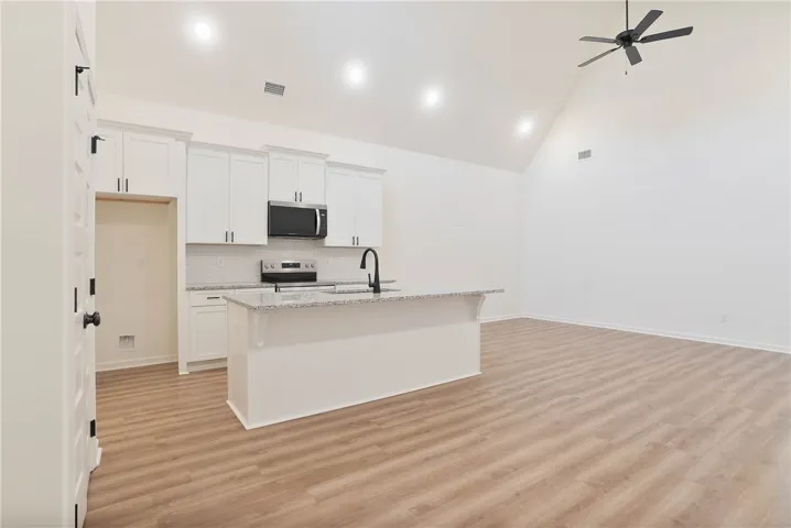 An open-concept living area features a contemporary kitchen island and high vaulted ceilings with a ceiling fan.