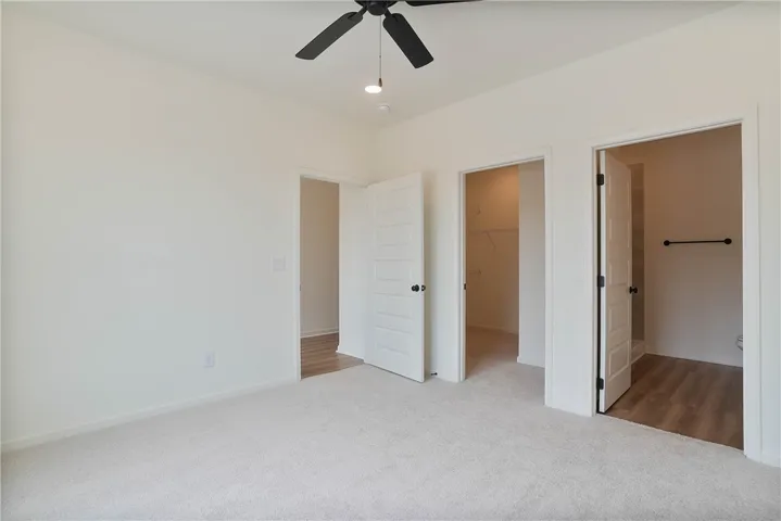 A spacious, newly finished room boasts clean carpeted flooring and a modern ceiling fan.