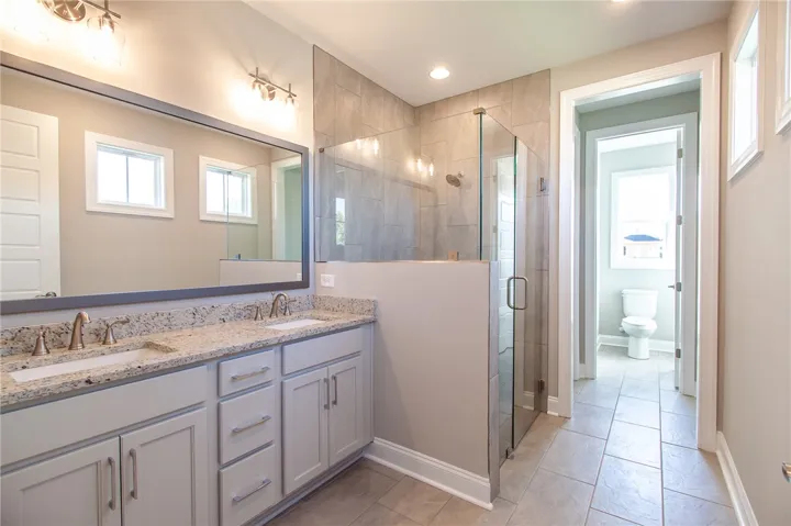 This spacious bathroom offers a double vanity and a sleek, glass-enclosed shower.