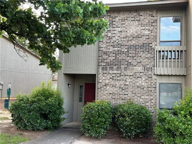 A well-maintained facade features brick and siding, complemented by neatly trimmed foundation plantings and a welcoming red entry door.