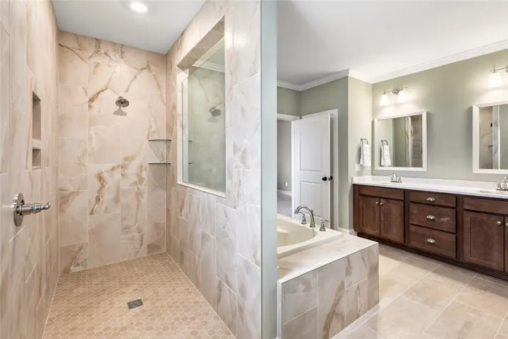 A glass partition divides the fully tiled shower from the tub deck, maintaining open sightlines and a cohesive design.