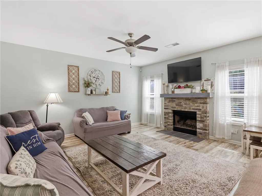 A comforting living area features a stone fireplace, light wood-look flooring, and a ceiling fan for year-round comfort.