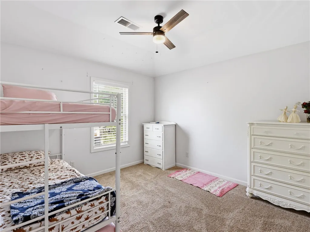A comfortable bedroom with soft carpet flooring and a ceiling fan, offering a bright and airy atmosphere.