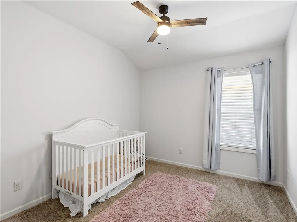 A well-lit bedroom with vaulted ceilings features a ceiling fan and ample natural light from a window.