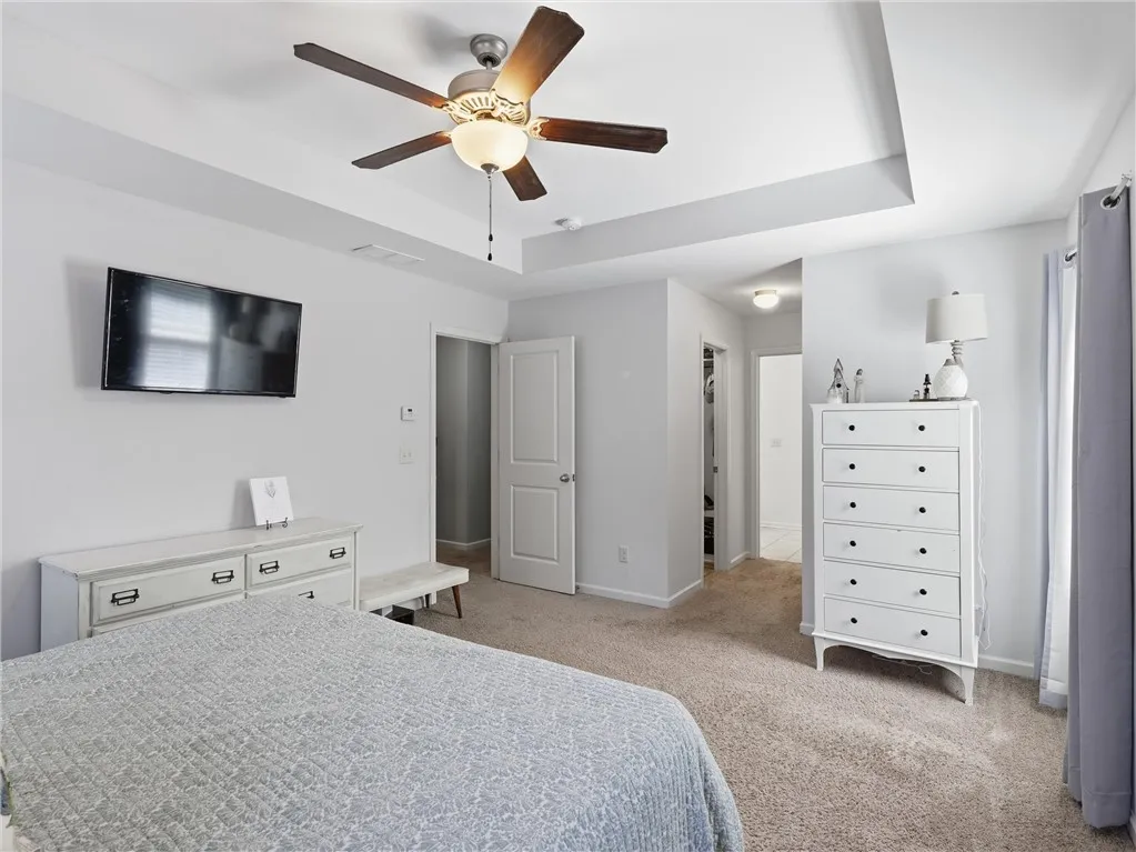 A restful primary bedroom retreat features a tray ceiling and a walk-in closet beyond.