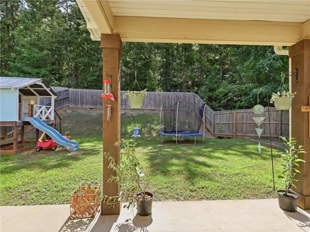 A fenced backyard offers a playful space with a trampoline and an elevated playhouse.