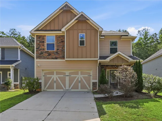 A welcoming facade presents a harmonious blend of siding and stone, complemented by an integrated garage and a neatly manicured lawn.