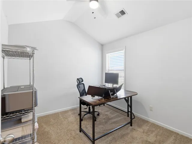 A well-lit home office features a vaulted ceiling and a functional workstation.