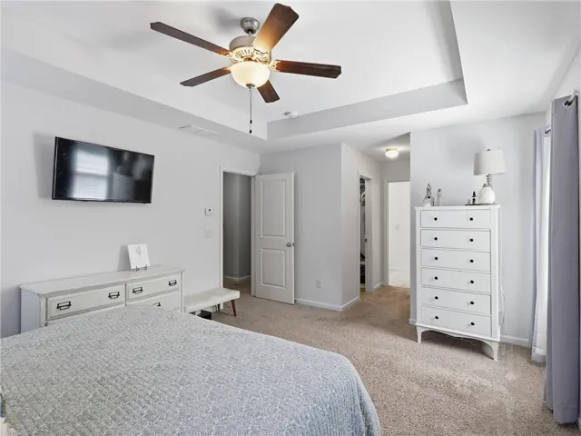 A restful primary bedroom retreat features a tray ceiling and a walk-in closet beyond.