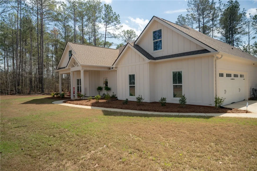 White siding and a gabled roof characterize this appealing home with a forest backdrop.