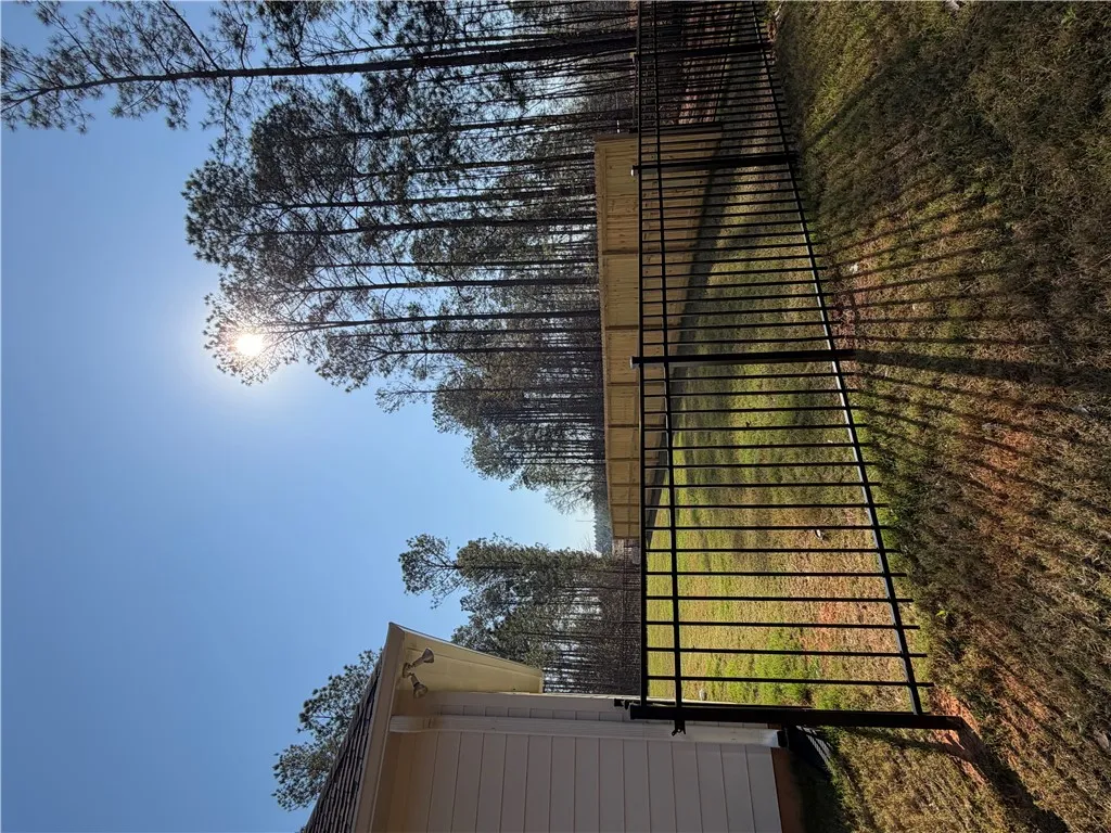 Secure yard featuring a tall black metal fence and mature trees under a clear sky.