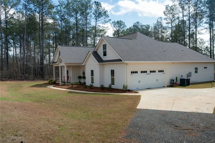 A striking contemporary farmhouse design with an attached garage, nestled against a backdrop of mature pine trees.