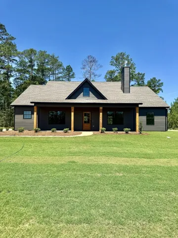 A modern farmhouse design with a deep, welcoming front porch and natural wood pillars anchors this verdant lot.
