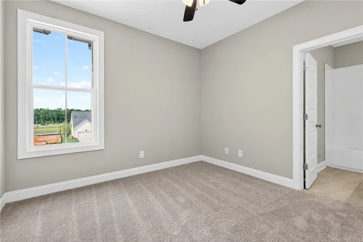 A well-lit bedroom features plush carpeting, a wide window with natural light, and convenient access to an adjacent bathroom.