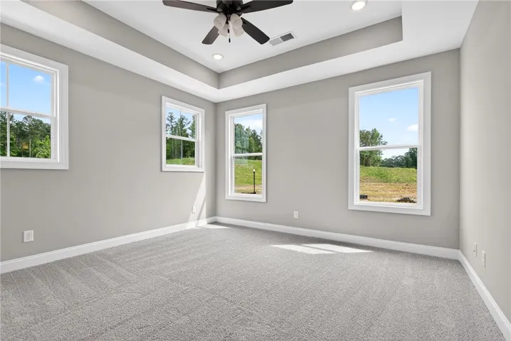 A spacious bedroom features multiple windows that invite abundant natural light and showcase serene green views.