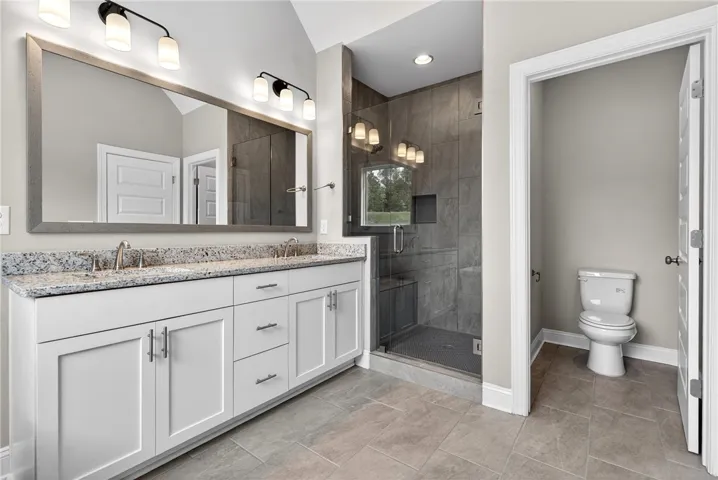A well-appointed primary bathroom showcases a double vanity with granite counters and a spacious glass-enclosed shower.