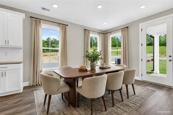Natural light pours into this elegant dining area, boasting rich hardwood flooring and a pristine white kitchen cabinet system.
