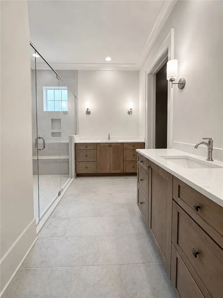 Fine tile flooring and dual vanities anchor this beautifully crafted bath space with glass-enclosed shower.