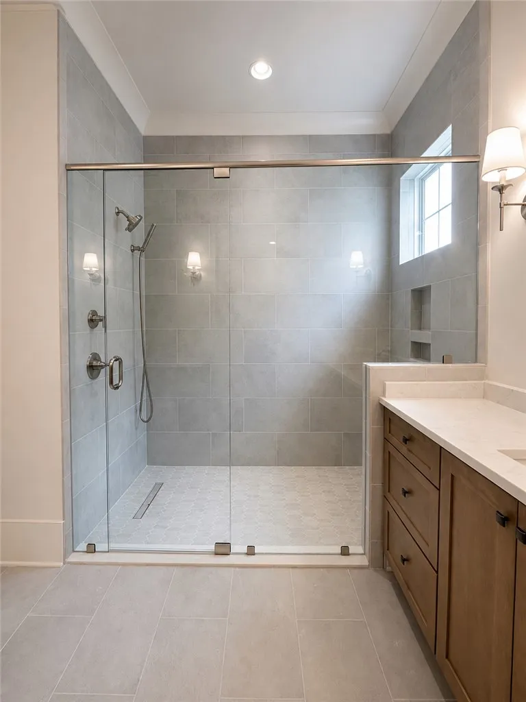 A spacious walk-in shower features floor-to-ceiling tiling, glass enclosure, and modern stone-topped vanity.
