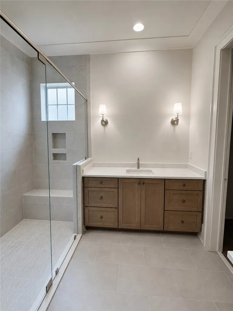 A glass-enclosed walk-in shower sits adjacent to a wood vanity with stone counters.