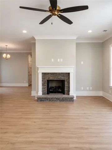 A stone fireplace anchors this living space, featuring blonde wood flooring and a modern ceiling fan.