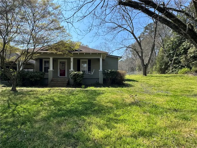 This charming home offers a welcoming facade with a large, verdant lawn and mature trees.
