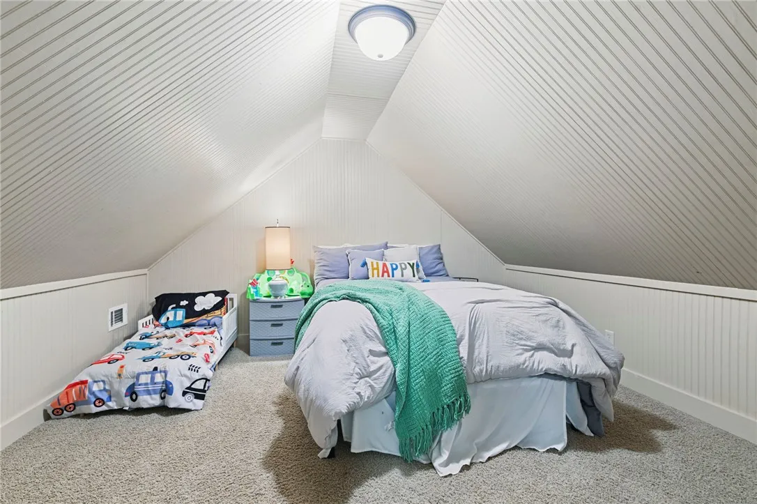 A cozy bedroom space with sloped ceilings and ample carpeted floor area.