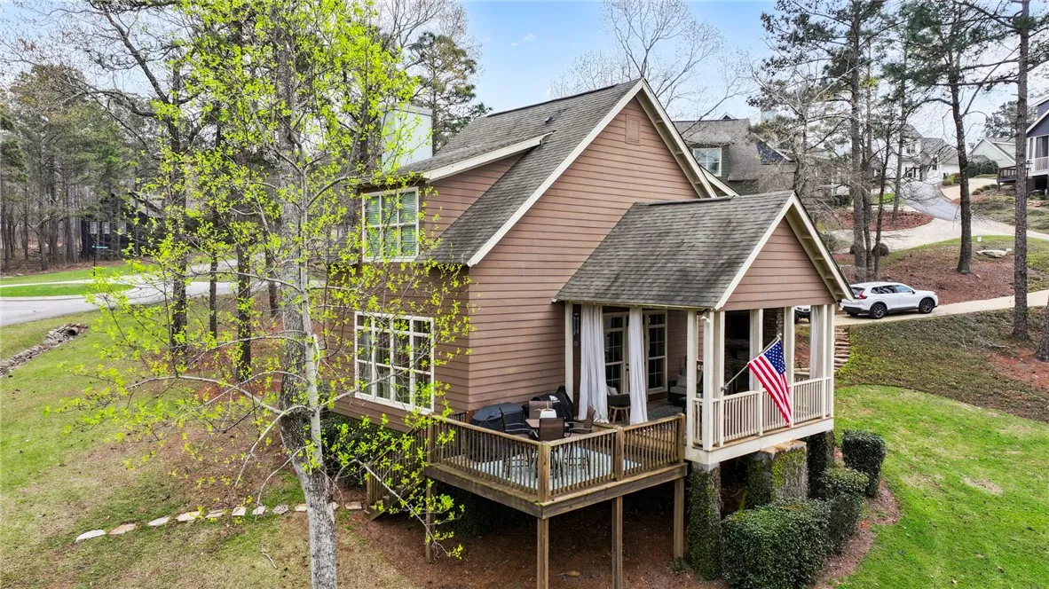 An inviting rear facade with a covered patio and open deck, nestled amidst lush trees and natural landscaping.