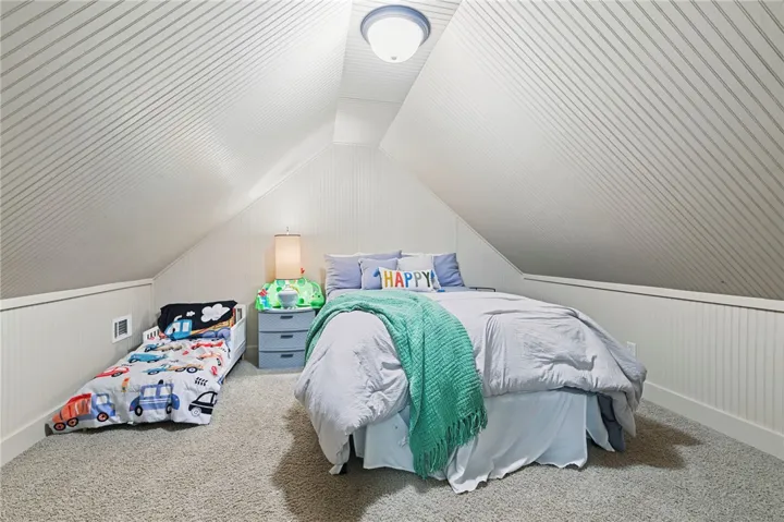 A cozy bedroom space with sloped ceilings and ample carpeted floor area.