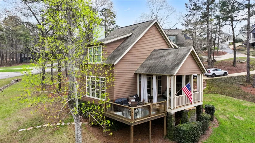 An inviting rear facade with a covered patio and open deck, nestled amidst lush trees and natural landscaping.