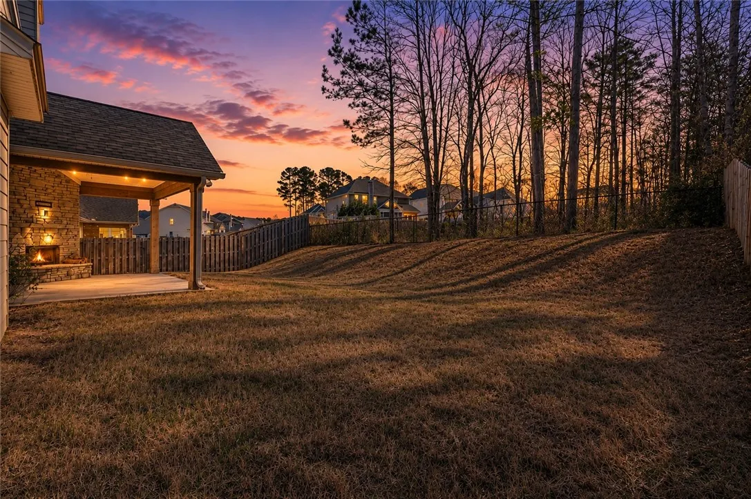 An inviting covered patio with a built-in fireplace awaits, perfect for twilight gatherings under a vibrant sky.
